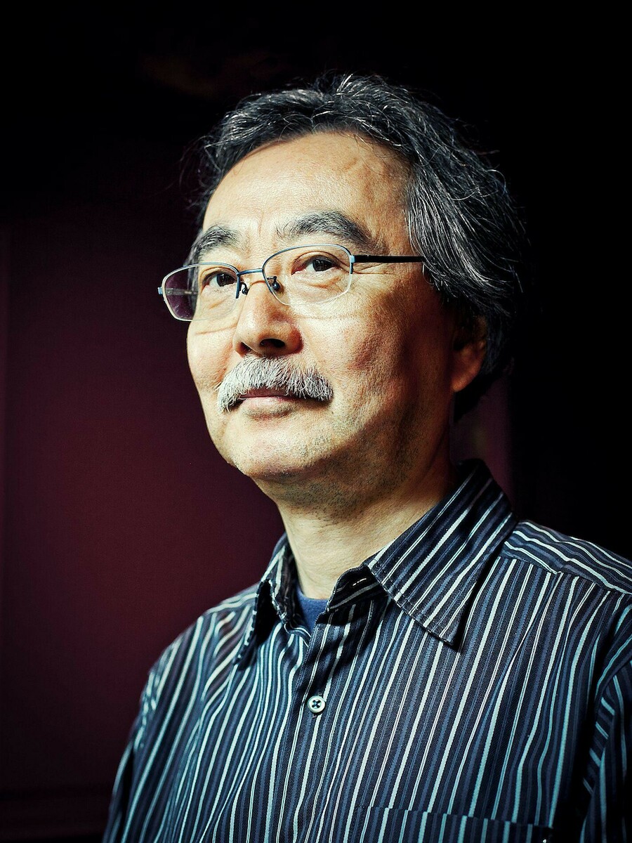 Portrait de Jirō Taniguchi, portant des lunettes et une chemise à rayures